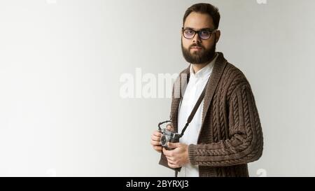Confident hipster photographer with camera on a strap posing isolated on white background. Model wearing warm brown sweater and has a beautiful black Stock Photo