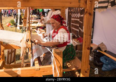Old Women in Traditional Folk Costume Called 'Kroj' Making Traditional Hand Made Knotted Runner Carpet On Wooden Loom. Stock Photo