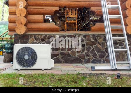 New modern HVAC air conditioning external compressor unit preapred for installation or replacement near wall of wooden log residential country cottage Stock Photo