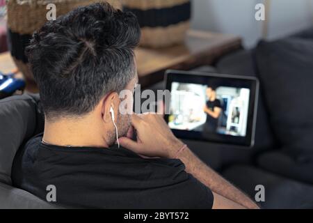 man hand holding using digital tablet watching online cooking master class using headphones. learning cooking remotely Stock Photo