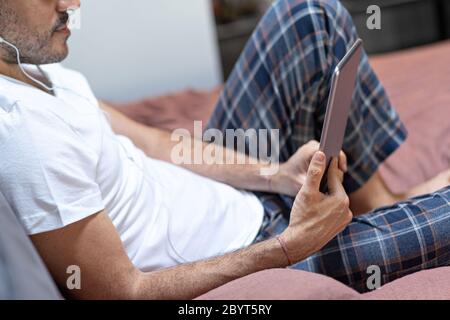 man holding using digital tablet and headphones in bed at home with pijama. Online education, working, video call Stock Photo