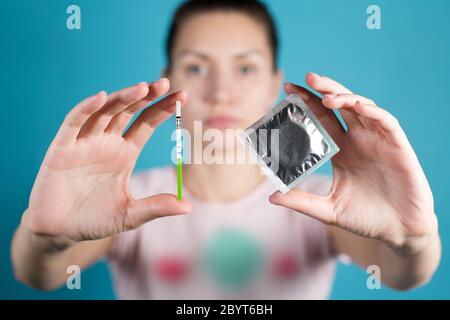 A young girl holds out a condom and a positive pregnancy test Stock Photo