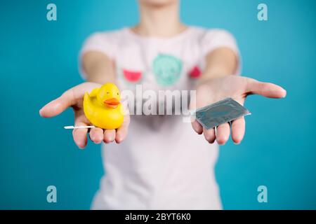 A young girl holds out a condom and a toy duck with a pregnancy test Stock Photo