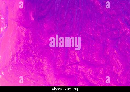Background from purple recyclable polyethylene in neon pink light. Eco, zero waste, alternative to plastic concept. Flat lay. Horizontal. Closeup. Stock Photo