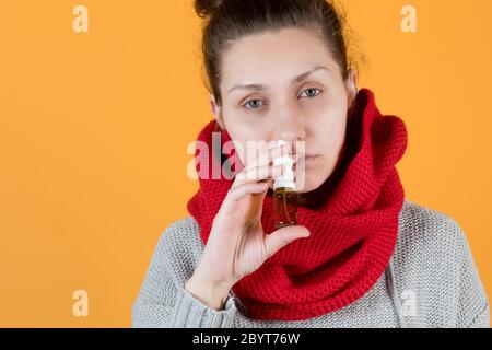 A young woman of a sickly look sprays a cure for colds and flu in her nose. Stock Photo