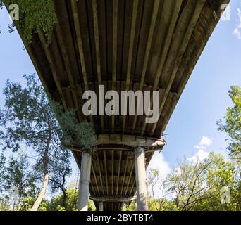 Under the bridge. Look up on old rusty construction in green trees on blue sky background Stock Photo