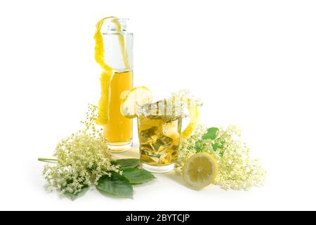 Elderflower syrup in a bottle and homemade lemonade in a drinking glass, lemon zest and slices and some fresh blossoms, isolated on a white background Stock Photo