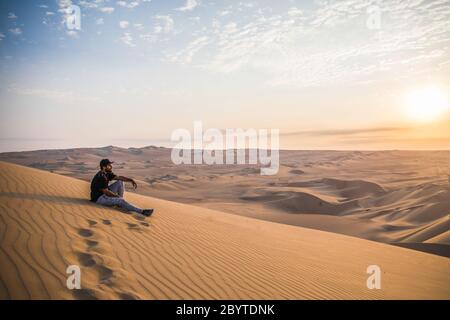 man sitting on a top of a dune, footprints, clouds and sunset Stock Photo