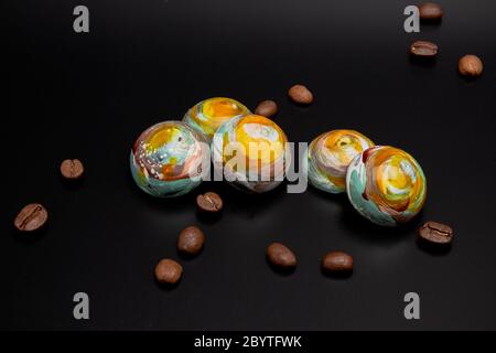 Staked colorful round milk chocolates that looks like planets isolated on black background with copy space, roasted brown coffee beans around them Stock Photo