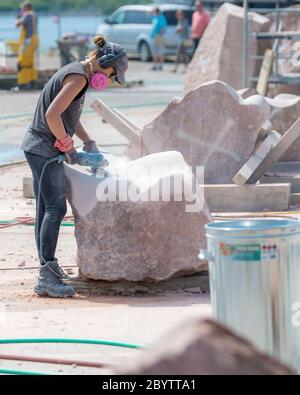 An artist works on a large block of stone at Sculpture Saint John, a sculpture symposium that hosts artists from around the world. Stock Photo