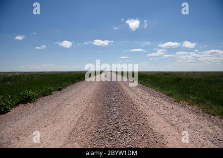 A deserted rural country dirt road through fields with sky and clouds leading to the horizon Stock Photo
