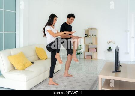 Young Asian couple doing High-intensity interval training together and looking TV at home, man and woman working out together standing in living room, Stock Photo