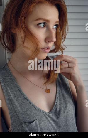 A red-haired girl stands in a half-turn and looks into the distance, holding the tip of a braid with her hand. Stock Photo