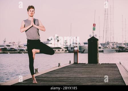 Young redhead practicing yoga, Vriksasana tree posture, to concentrate and help him with his mindfullness Stock Photo