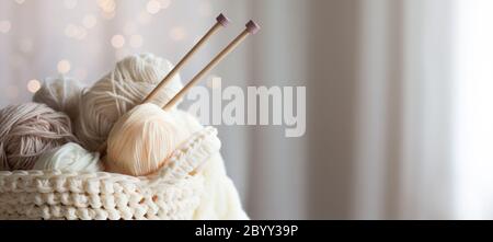 Knitted white and beige fabric. Woolen and cotton yarn lies in a basket. Glasses lie on a white wooden background. Stock Photo