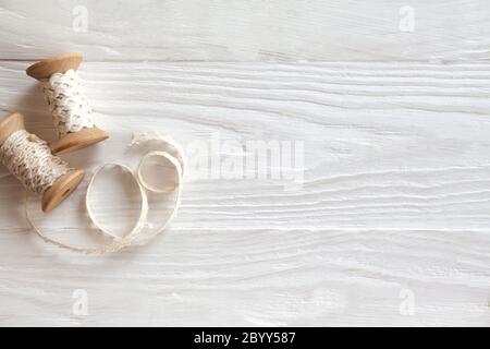 Old-style white lace is wound on wooden spools. Vintage accessories for sewing. White wood background. Stock Photo