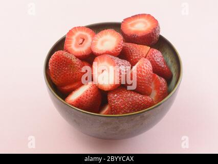 Ceramic bowl of freshly cut raw strawberries on pink background Stock Photo
