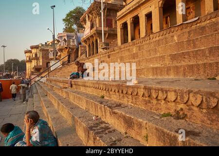 Devotees and travelers sit on the steps of Riva Ghat, facing the rising sun early in the morning in the banks of Ganga at Varanasi. Stock Photo