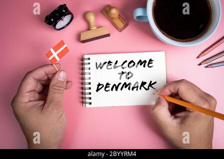 WELCOME TO DENMARK. Coffee mug, wooden stamps and stationery on a pink table Stock Photo