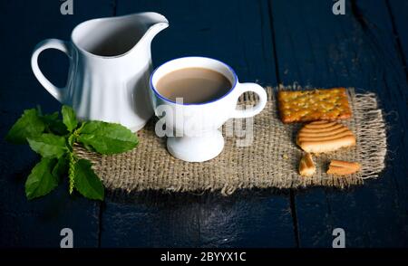 A cup of tea with tasty biscuits, teapot and fresh Leaves on old wooden dark background Stock Photo