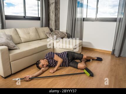 Man who was sweeping the living room of his house and fell asleep on the floor. Full body. Stock Photo
