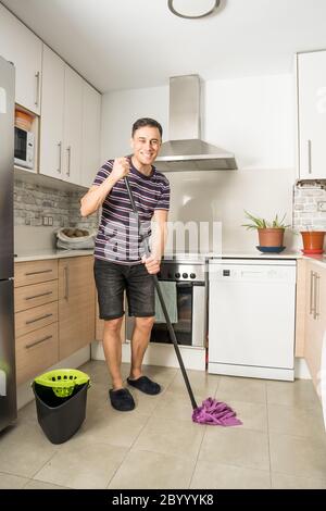 Smiling man wearing casual clothes and slippers mopping the kitchen floor. Full body. Stock Photo