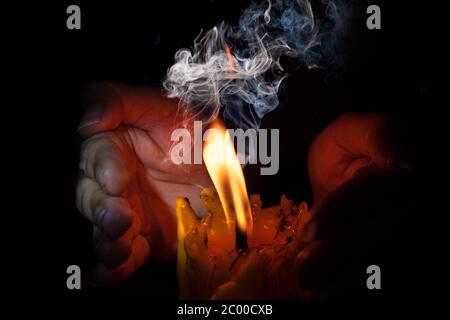 Hand protecting candle light from the wind in darkness on black background Stock Photo