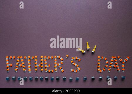 Congratulation on Father's Day composed of transistors and microcircuits on a brown background. Flat composition with the phrase HAPPY FATHER DAY. Stock Photo
