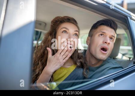 Very surprised man and woman looking out of the car. Stock Photo