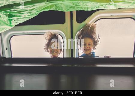 Children, having fun in motorhome while heavy raining outdoors, playing and making mischiefs together, hanging upside down Stock Photo