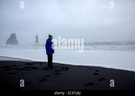Children running from and to the ocean in black sand beach of Reynisfjara and the mount Reynisfjall in Iceland on a cold winter rainy day