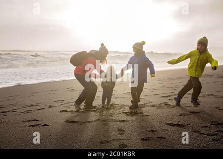 Family posing against the sun in black sand beach of Reynisfjara and the mount Reynisfjall in Iceland on a cold winter day