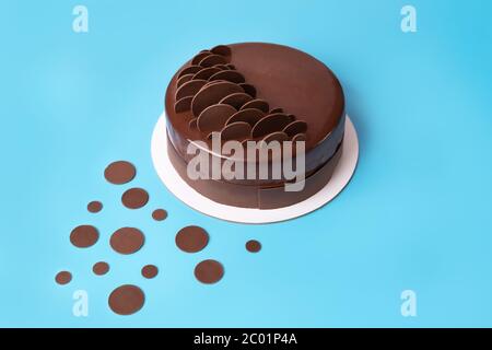 Dark chocolate mousse cake covered with mirror glaze and decorated with round chocolate chips on blue background. Modern stylish cake. Close-up. Copy Stock Photo