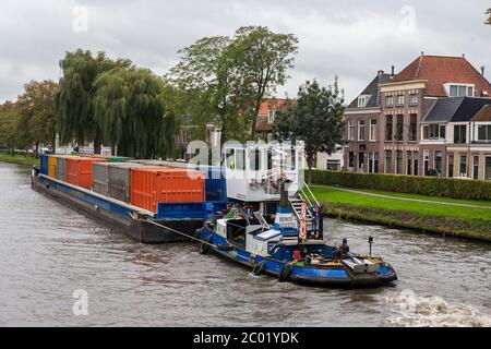 Tug pushing a lighter loaded with containers, navigating the Rijn-Schiekanaal in Delft, and leaving the Koepoort Bridge, Delft, South Holland, Netherl Stock Photo