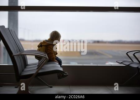 Blonde toddler boy with family, traveling with airplane, running at the airport with suitcase Stock Photo