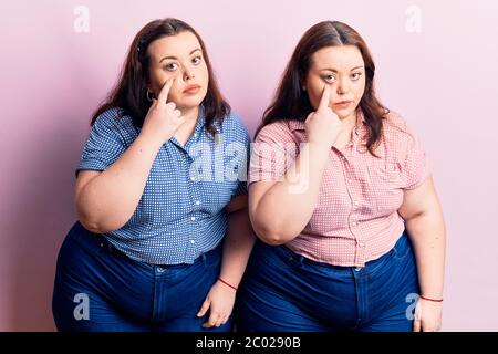 Young plus size twins wearing casual clothes pointing to the eye watching you gesture, suspicious expression Stock Photo