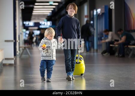 Blonde toddler boy with family, traveling with airplane, running at the airport with suitcase Stock Photo