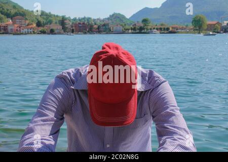 Man in cap relaxing against lake and mountains Stock Photo
