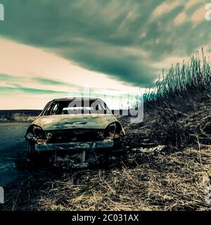 Abandoned car on the side of the road with grass verge, puddles and sky - 'End of the Road' Stock Photo
