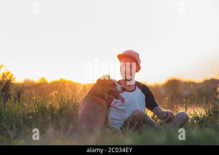 Man interacts with his dog in sunset, summer season. Pets and human friendship, taking care, spending time together. Stock Photo