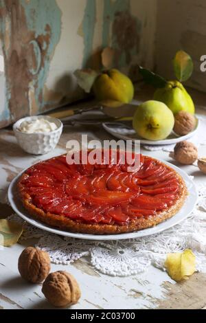 Quince tarte tatin served with whipped cream, quince fruits and walnuts on a wooden surface. Rustic style. Stock Photo