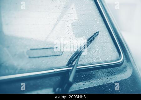 The black windshield wiper on the back window of the car, which is wet from raindrops on a quiet, cloudy, foggy day. Melancholy. Bad weather. Stock Photo