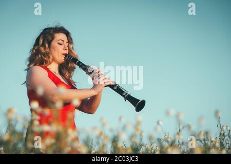 woman in a red dress playing the clarinet in a field of daisies Stock Photo