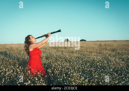 woman in a red dress playing the clarinet in a field of daisies Stock Photo