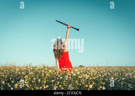 woman in a red dress raising a clarinet in a field of daisies Stock Photo