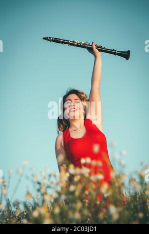 woman in a red dress raising a clarinet in a field of daisies Stock Photo