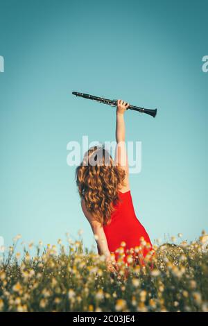 woman in a red dress raising a clarinet in a field of daisies Stock Photo