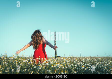 woman in a red dress and a clarinet enjoying freedom in a field of daisies Stock Photo