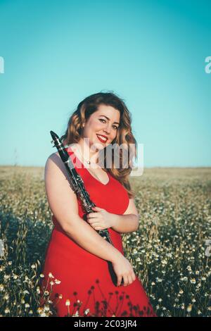 woman in a red dress playing the clarinet in a field of daisies Stock Photo