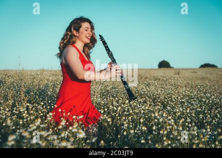 woman in a red dress playing the clarinet in a field of daisies Stock Photo